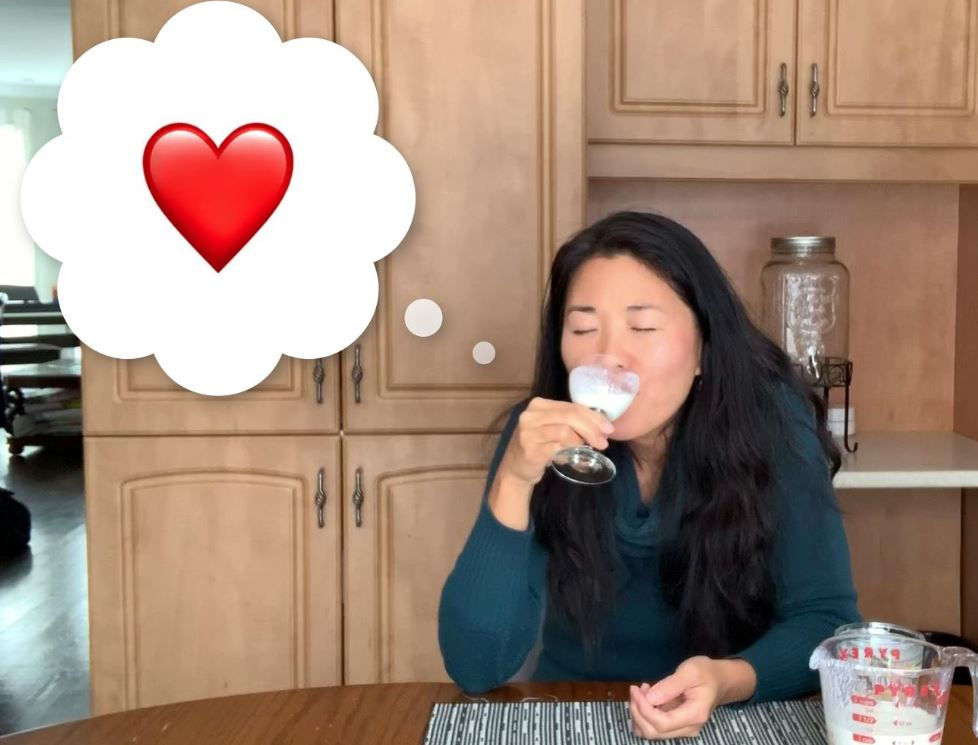 Cindy drinking kefir with eyes closed looking happy with a heart inside a thought cloud implying that she loves this drink!